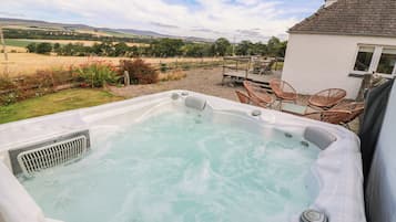 A hot tub with a view of a rural landscape, surrounded by wicker furniture.