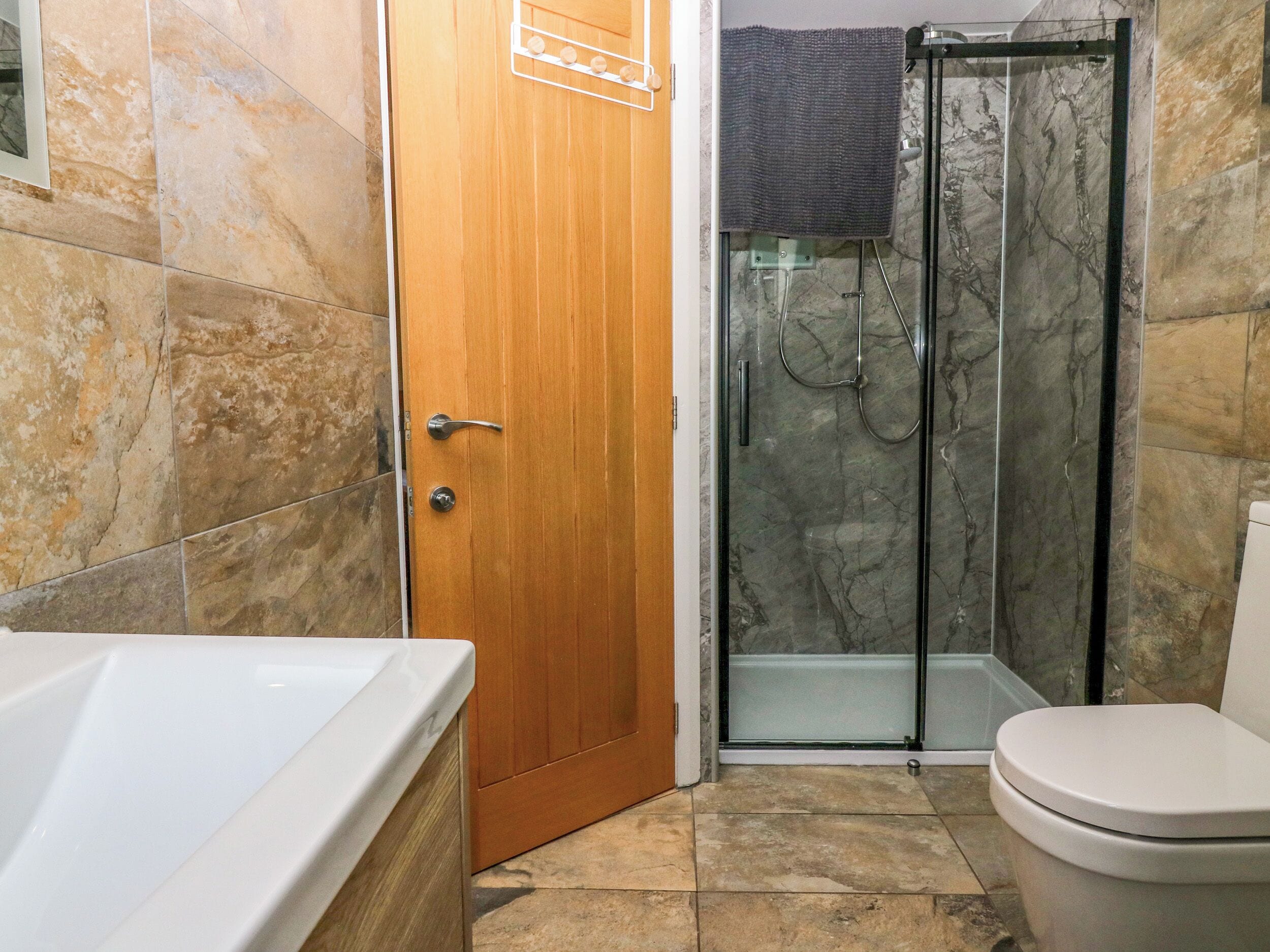 Un baño con puerta de madera, cabina de ducha de vidrio, bañera blanca y un inodoro.
