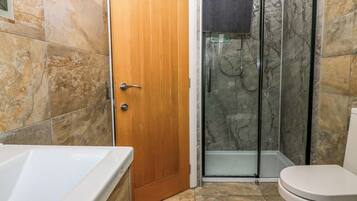 Un baño con puerta de madera, cabina de ducha de vidrio, bañera blanca y un inodoro.