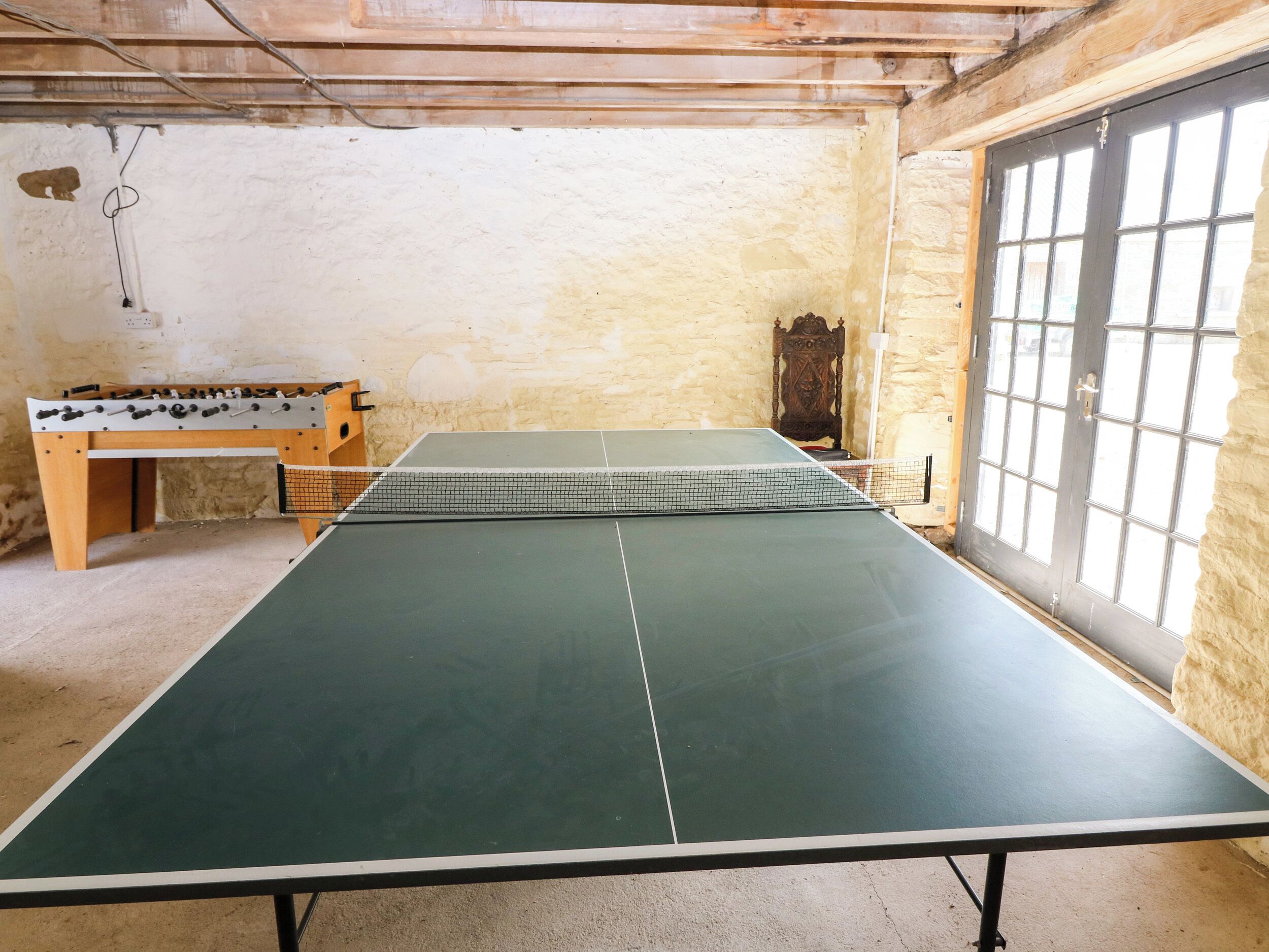 Una mesa de ping pong con red en una habitación con paredes de piedra y una mesa de madera.