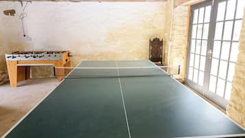 Una mesa de ping pong con red en una habitación con paredes de piedra y una mesa de madera.