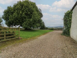 A gravel driveway leading to a white building with a wooden gate on the left.