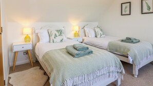 Un dormitorio con dos camas, cada una con una colcha verde y blanca estampada, almohadas blancas y una mesita de noche con una lámpara amarilla.