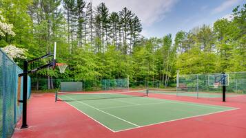 A tennis court with a net, surrounded by trees and a fence.