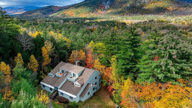 A two-story house with a sloped roof, surrounded by dense forest and autumn foliage. - Inviting Bartlett Condo: 1 Mi to Attitash Mountain (Bartlett)