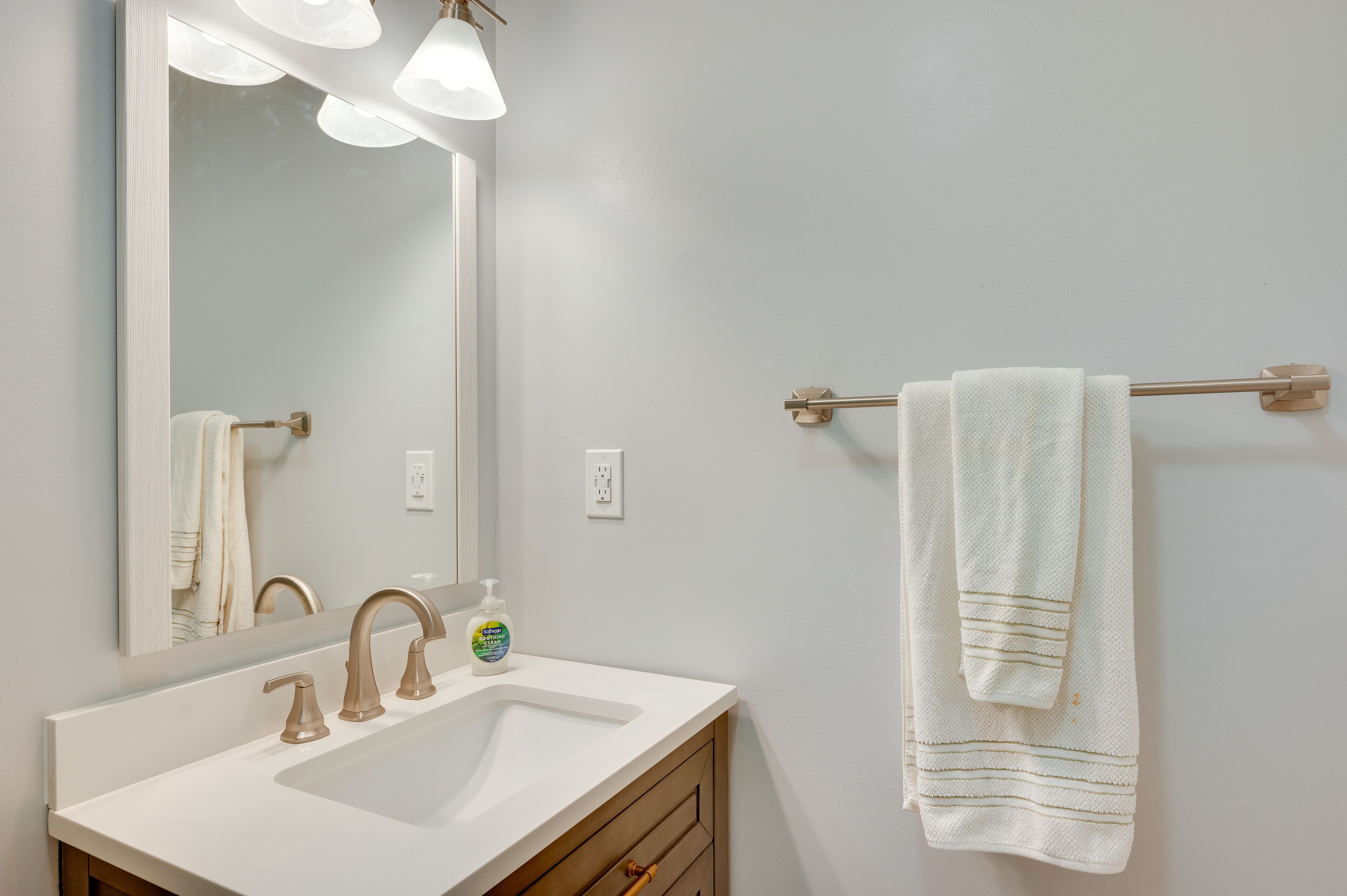Un bagno con lavandino bianco, uno specchio e un portasciugamani con un asciugamano.
