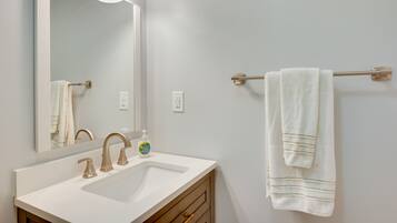 Un bagno con lavandino bianco, uno specchio e un portasciugamani con un asciugamano.