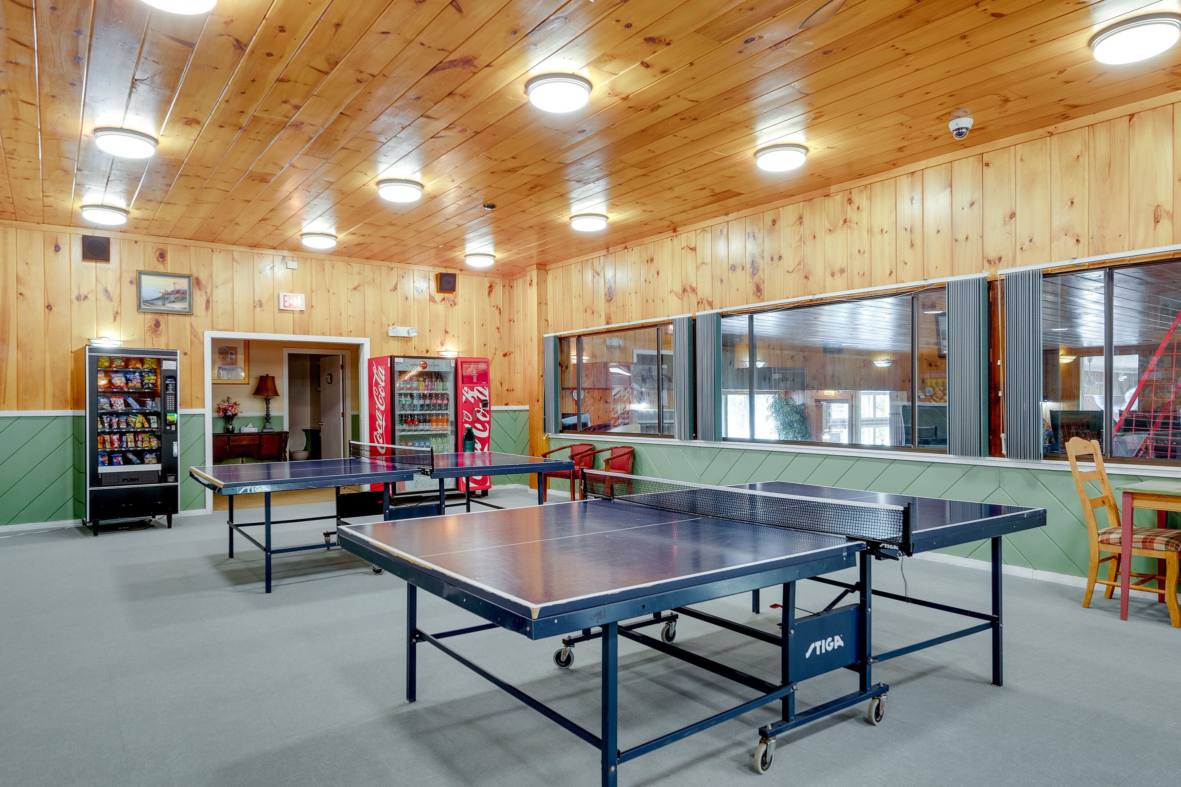 A room with wooden walls, a ping pong table, a Coca-Cola refrigerator, and a vending machine.