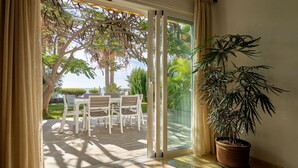 A sliding glass door leading to an outdoor patio with a table and chairs, a potted plant, and a view of greenery and a body of water.