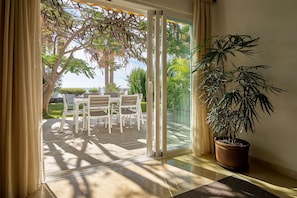 Habitación con puerta de vidrio corredera que da a un patio exterior con mesa y sillas, y una planta en maceta en el suelo.