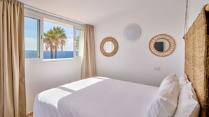 A bedroom with a bed, two wall mirrors, a window with curtains, and a view of palm trees.