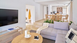 A modern living room with a TV, sofa, coffee table, and dining area with chairs.