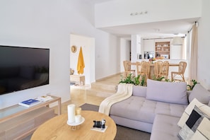Una sala de estar moderna con un televisor de pantalla plana, una mesa redonda de madera y un sofá gris.