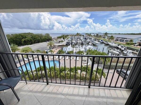 Een balkon met uitzicht op een jachthaven, een zwembad en een gebouw in de verte.