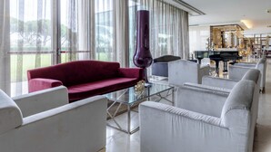 Un salon moderne avec un canapé rouge, des fauteuils blancs, une table basse en verre et un grand piano.