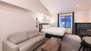 A modern hotel room with a large bed, a sofa, a wooden coffee table, and a fireplace. - Hearthstone Lodge #406 | 3 Peaks Rentals (Sun Peaks)