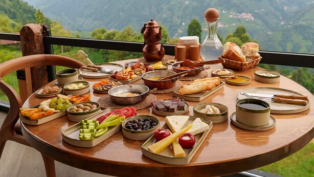 Een tafel gedekt met diverse gerechten en een koperen pan, met uitzicht op een bergachtig landschap.