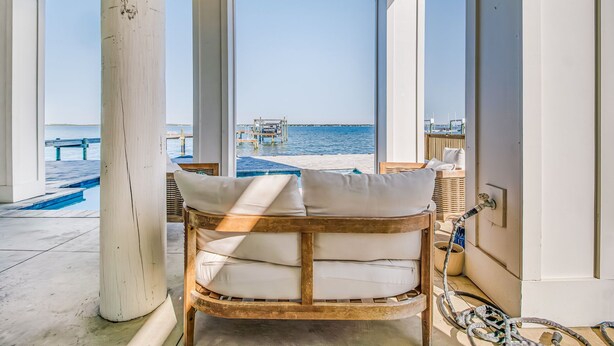 Una silla de mimbre con cojines en una habitación con ventanas amplias que dan a una piscina y al mar.