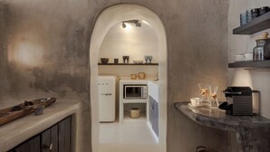 Una cocina estrecha con microondas, un refrigerador y un armario de madera. Hay estantes con utensilios de cocina y una cafetera.