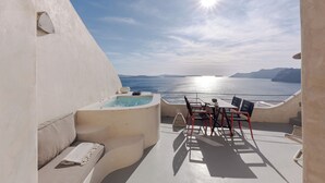 Un área de estar al aire libre iluminada por el sol, con un jacuzzi, una mesa y sillas, con vista a un cuerpo de agua.