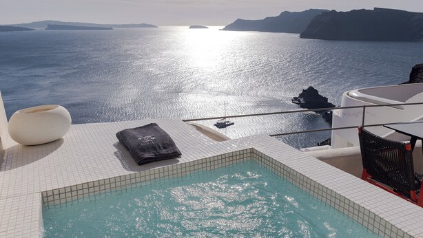 Un área de piscina con vista al mar, un jarrón blanco y una toalla negra.