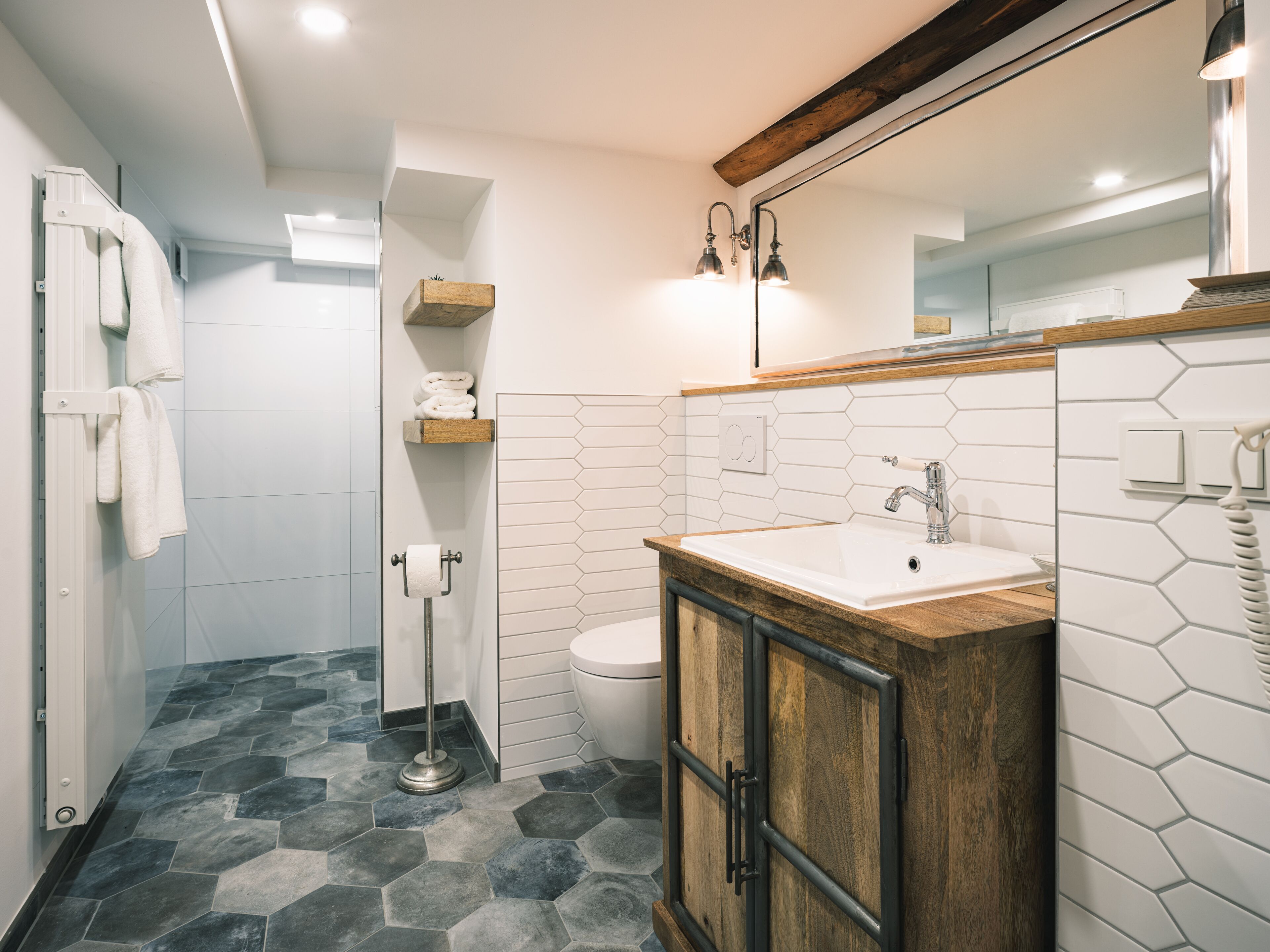Un baño moderno con inodoro blanco, tocador de madera con lavabo y zona de ducha.