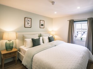 A neatly arranged bedroom with a bed, two bedside lamps, a nightstand, and a window with curtains. - Flecker Hotel (Freudenberg)