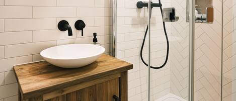 A modern bathroom with a wooden vanity, a round mirror, and a glass-enclosed shower area.