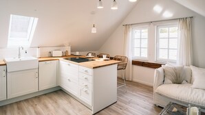 A modern kitchen with a central island, wooden flooring, and a dining area with a sofa and table. - Flecker Hotel (Freudenberg)