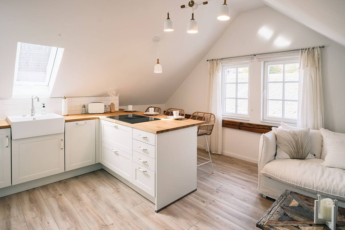 A modern kitchen with a central island, wooden flooring, and a dining area with a sofa and table.