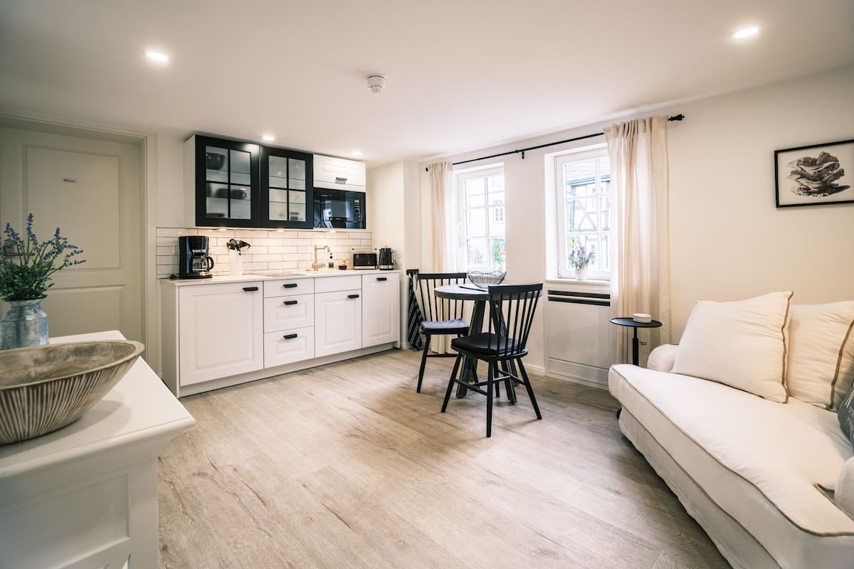 A modern kitchen with white cabinetry, a dining area with a table and chairs, and a white sofa in a bright living space.
