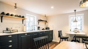 A modern kitchen with black cabinets, a wooden dining table, and a window with a view. - Flecker Hotel (Freudenberg)