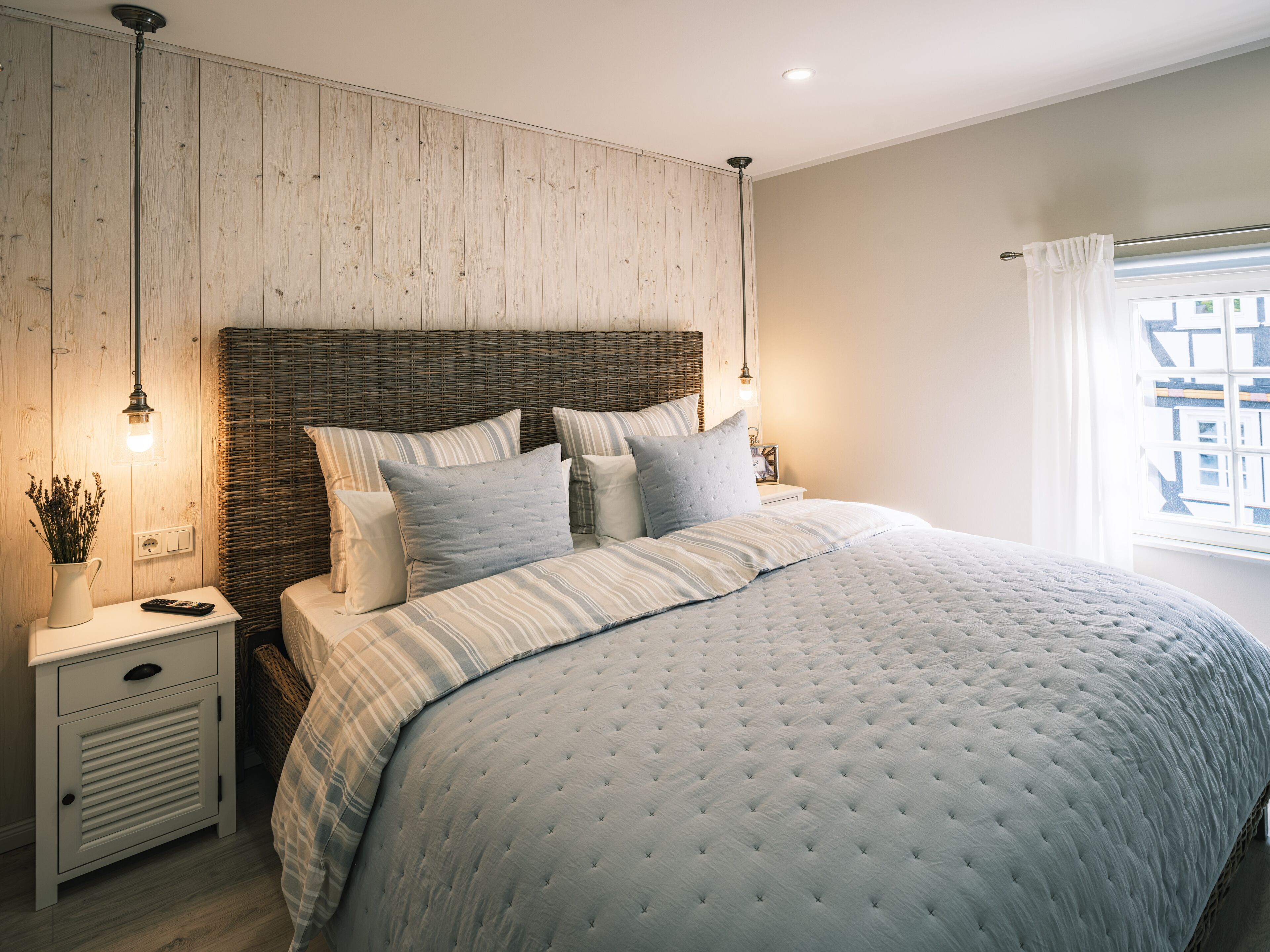 A bedroom with a large bed, a nightstand, a lamp, and a window with curtains.