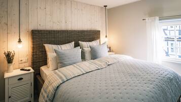 A bedroom with a large bed, a nightstand, a lamp, and a window with curtains.