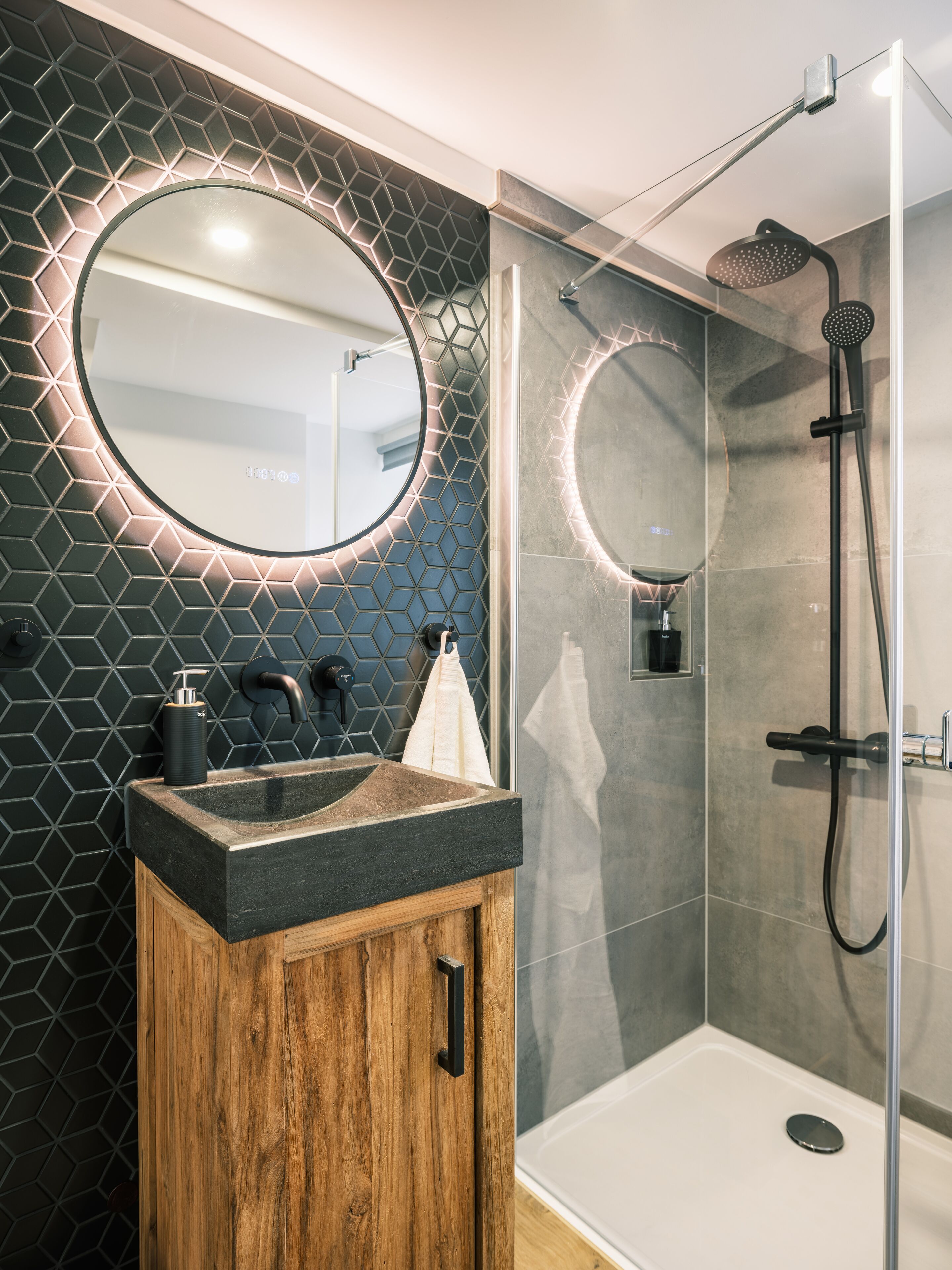 A modern bathroom with a round mirror, a wooden cabinet, and a glass-enclosed shower area.