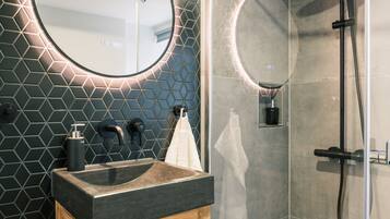 A modern bathroom with a round mirror, a wooden cabinet, and a glass-enclosed shower area.