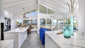 Eine moderne Küche mit einer großen Kochinsel, ein Essbereich mit blauen Sofas und Blick auf den Strand.