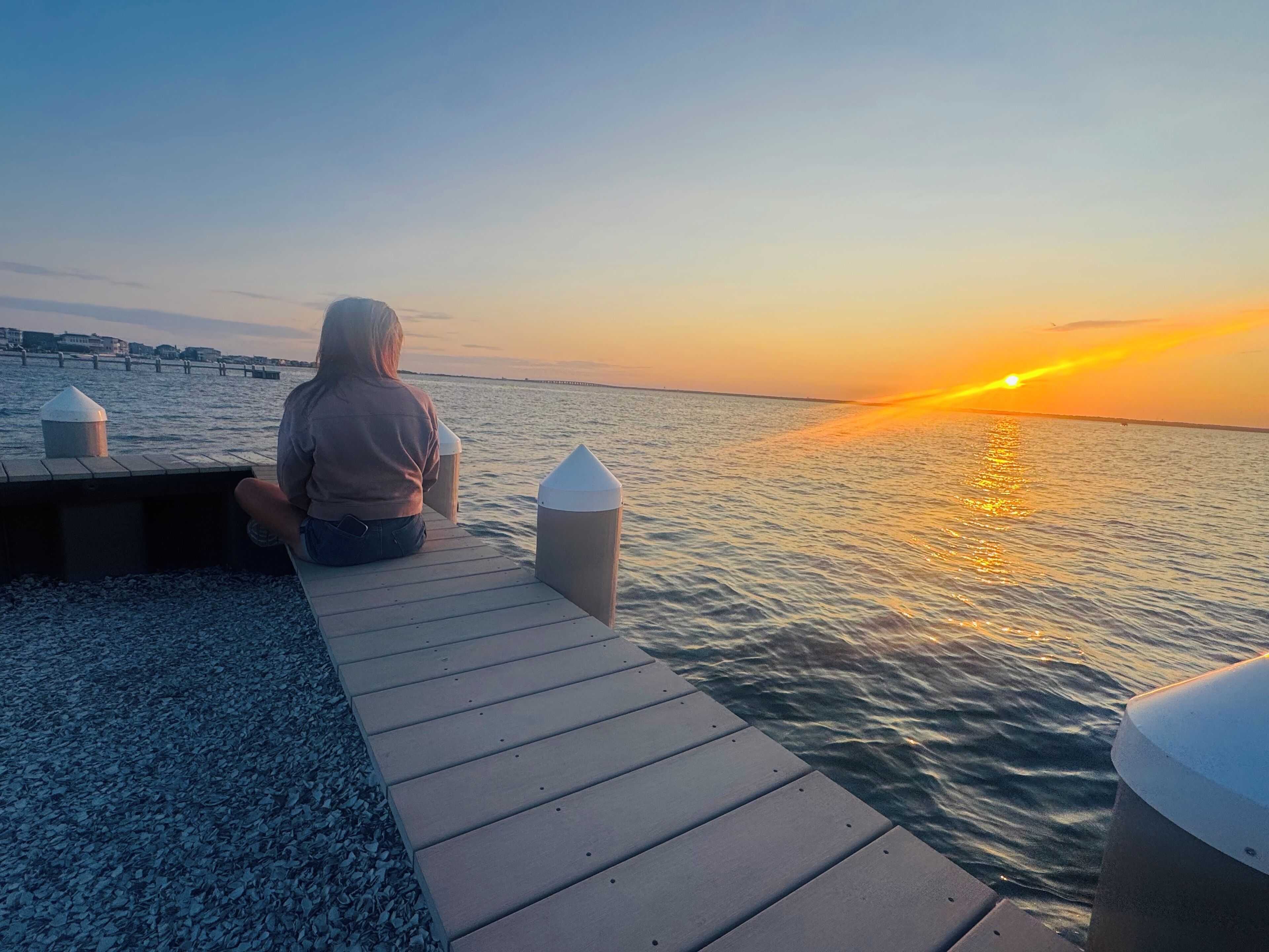 A person sitting on a wooden dock overlooking a body of water during sunset.