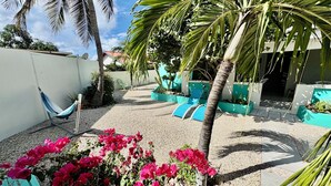 Une terrasse avec un hamac, des fauteuils de jardin bleus et un palmier.