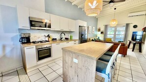 Une cuisine moderne avec des armoires blanches, un îlot central en bois et un ventilateur de plafond.