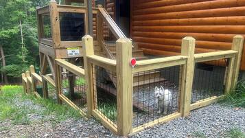 A wooden cabin with a fenced outdoor area and a staircase leading to a deck.