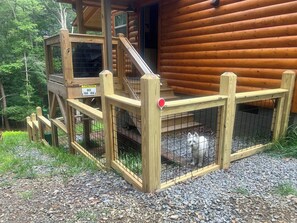 A wooden cabin with a fenced outdoor area and a staircase leading to a deck.