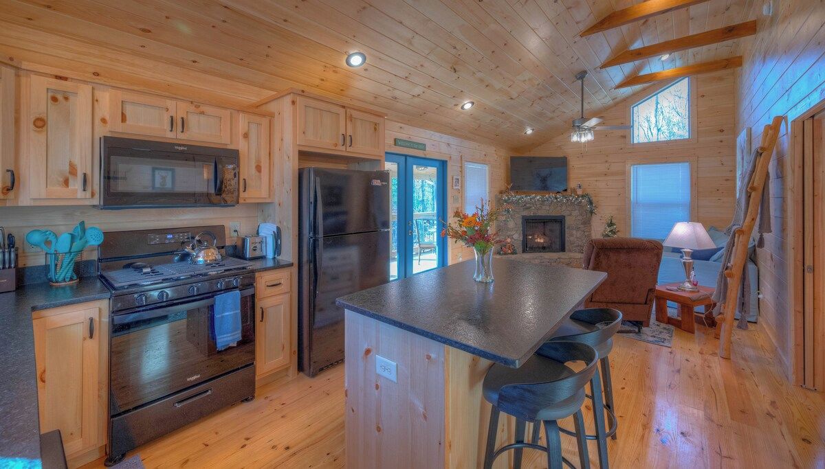 A wooden cabin interior with a kitchen featuring a stove, refrigerator, and microwave.