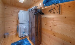 A compact room with wooden walls, a washing machine, a drying rack, and a small trash bin.
