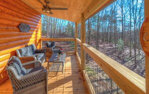 Una cabaña de troncos con terraza de madera, mobiliario de mimbre y vistas a un bosque.