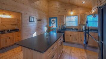 A wooden cabin interior with a kitchen area featuring a central island, wooden cabinets, and a refrigerator.