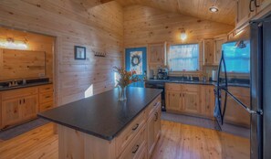 A wooden cabin interior with a kitchen area featuring a central island, wooden cabinets, and a refrigerator.