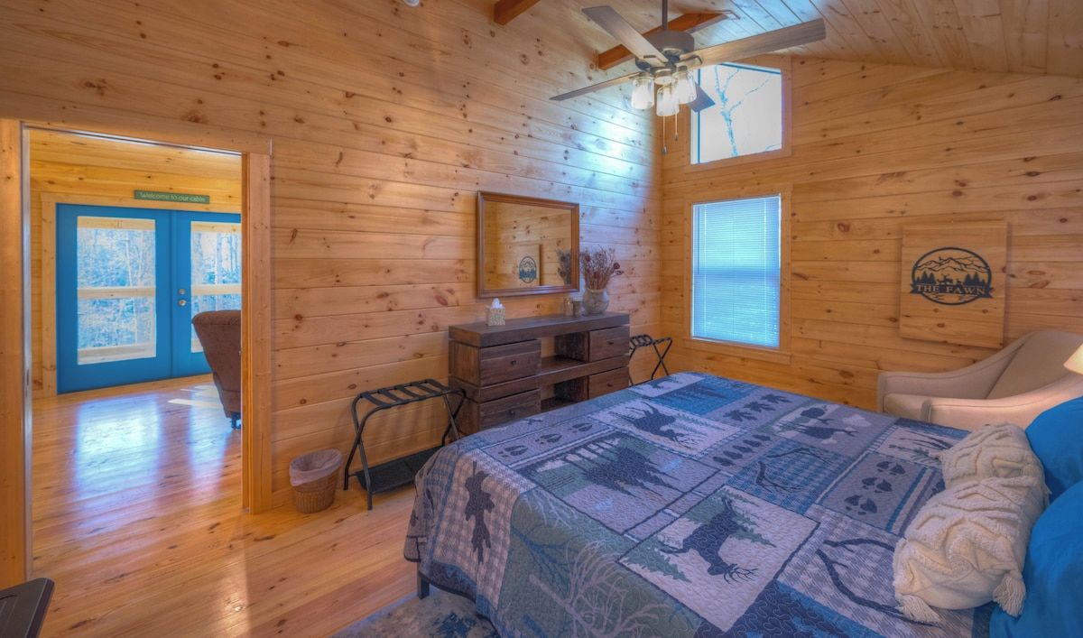 A wooden cabin room with a bed, dresser, and a ceiling fan.