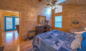 A wooden cabin room with a bed, dresser, and a ceiling fan.
