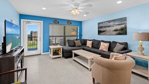 A living room with a dark grey sectional sofa, a beige armchair, a coffee table, a TV, and a ceiling fan.